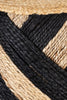 Close-up of handwoven jute pouf with natural and black braided stripes, highlighting eco-friendly texture for decor and seating needs.