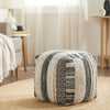 Black and white textured pouf with striped and patterned designs, placed on a round woven rug in a softly lit, cozy living room.