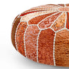 Close-up of a round patchwork pouf in orange, red, and beige tones with intricate patterns and white decorative stitching.