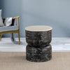 Black textured round table placed in a modern room, on a beige carpet with a soft blue wall and a green chair in the background.