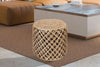 Black and tan jute pouf ottoman with crisscross pattern, placed in a modern living room setting featuring a brown rug and wooden table.