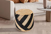 Round jute ottoman with natural beige and black diagonal stripes, placed on a light wooden floor next to a modern white sofa.