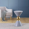 Modern hourglass-shaped gray side table with a gold metallic sphere in the center, placed on a wood floor and rug near an armchair.