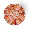 Top view of an orange and red patchwork pouf with white stitched accents, showcasing intricate radial patterns and vibrant textures.