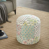 Colorful round pouf with intricate floral and geometric patchwork design, placed on a beige woven rug in a cozy living room corner.