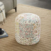 Round pouf with intricate floral patterns in pink, green, and yellow tones, placed on a textured beige rug in a cozy living room