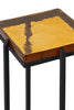 Close-up of a modern accent table featuring a square resin top with a golden wood grain pattern, supported by a sleek black metal frame.