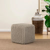 Square beige knitted pouf placed in a cozy living room setting, featuring woven decor and green plants in the background.