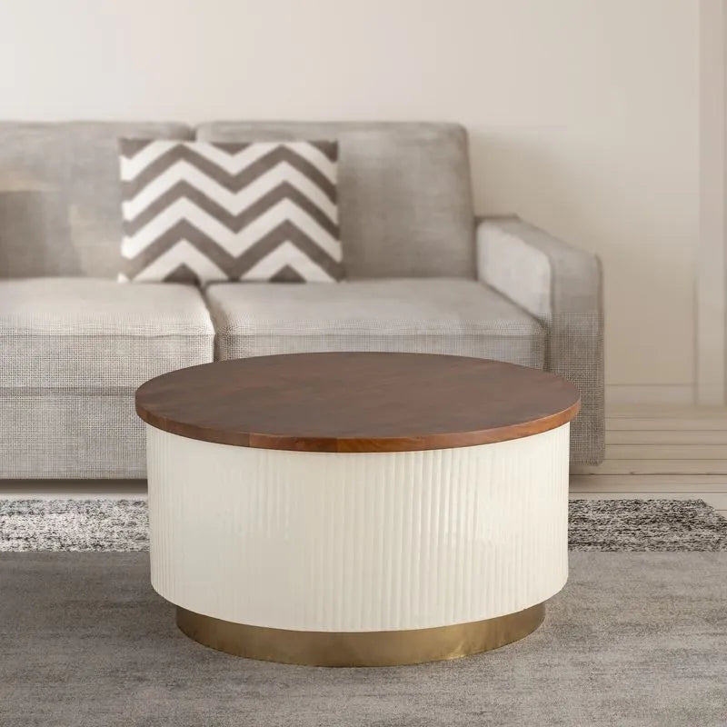 Modern round coffee table with a dark wood top, white textured base, and gold metal trim, placed in front of a gray sofa.