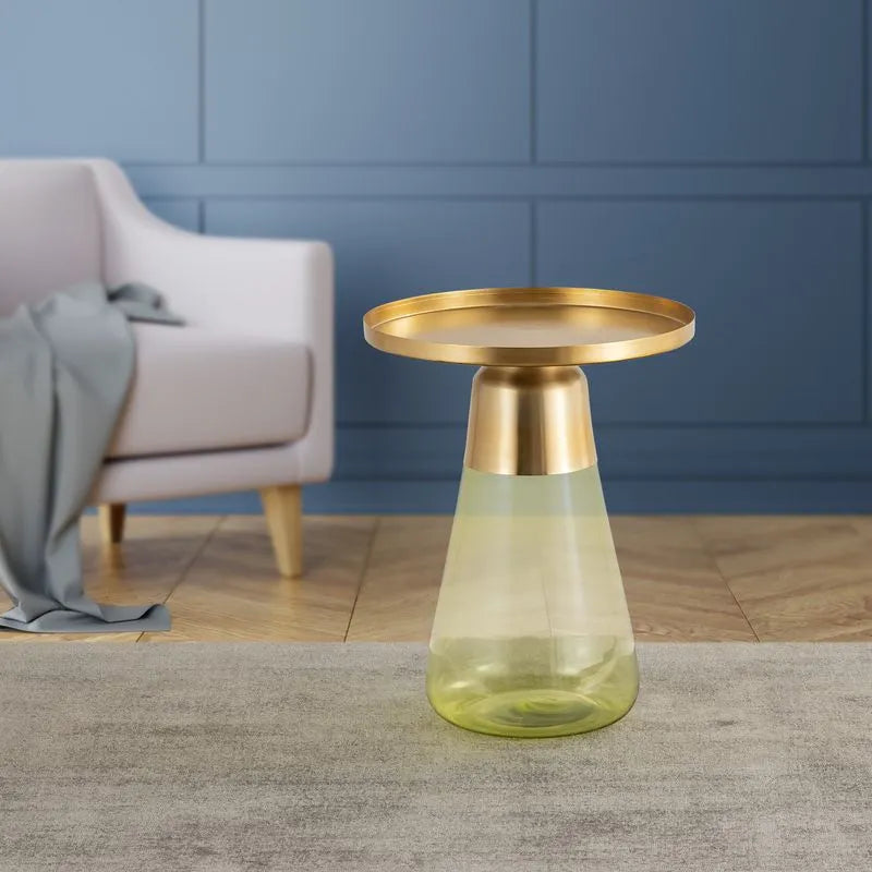 Modern table with a golden round top and a translucent green glass base, placed in a cozy living room with a blue wall backdrop.