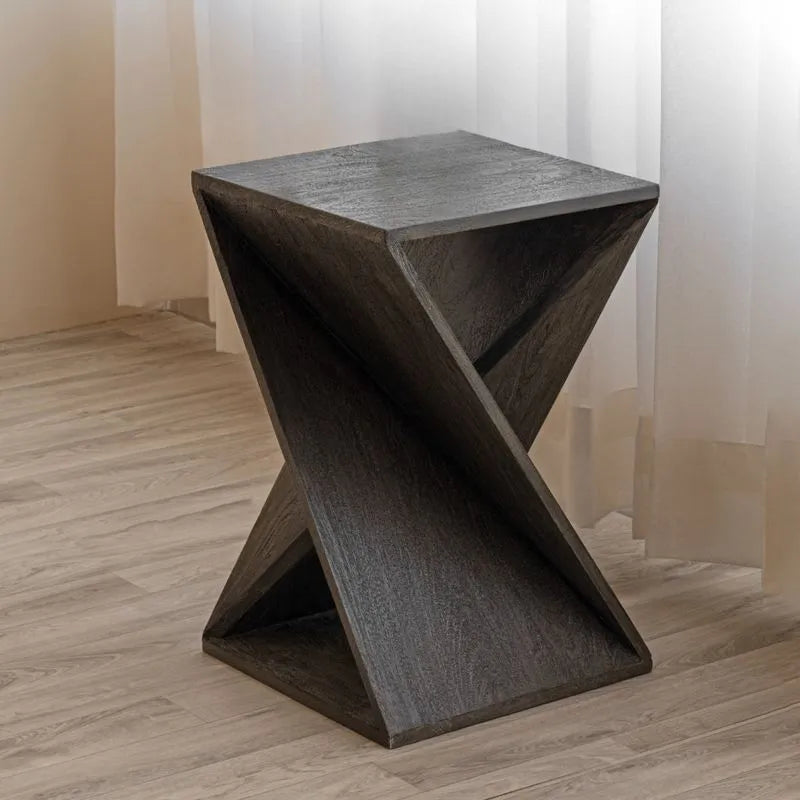 Gray twisted wood end table with a unique geometric design, placed on light wood flooring, positioned against sheer white curtains, perfect for decor accents.