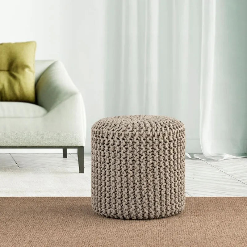 Albany Living cylindrical knitted pouf in light gray, positioned beside a minimalist white couch, perfect for modern, cozy decor.