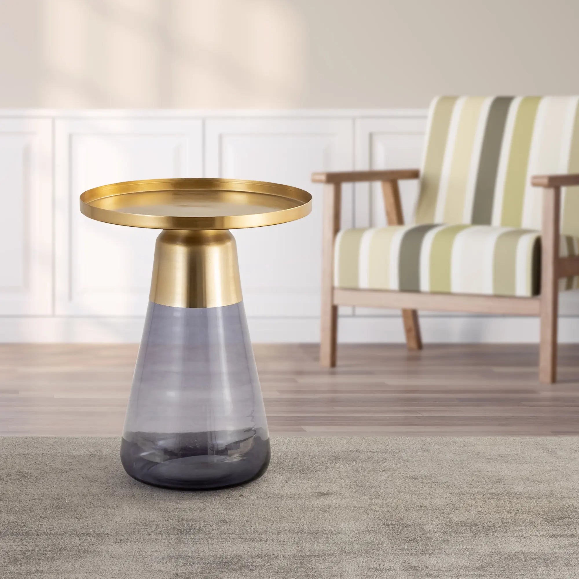 Elegant side table with a golden round top and a conical smoky gray glass base, displayed in a cozy living room setting.