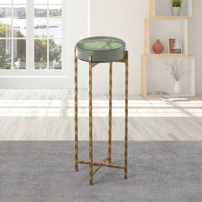 Green round accent table with gold legs, placed in a modern living room setup near a window.