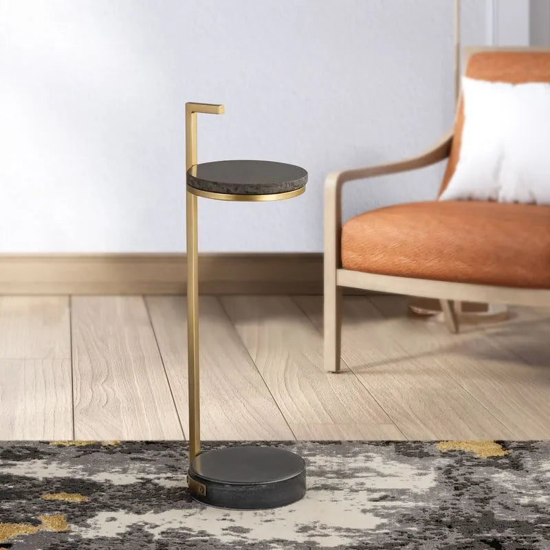 Gold-framed round side table with a black marble top placed beside an orange chair, creating a modern and cozy room accent.