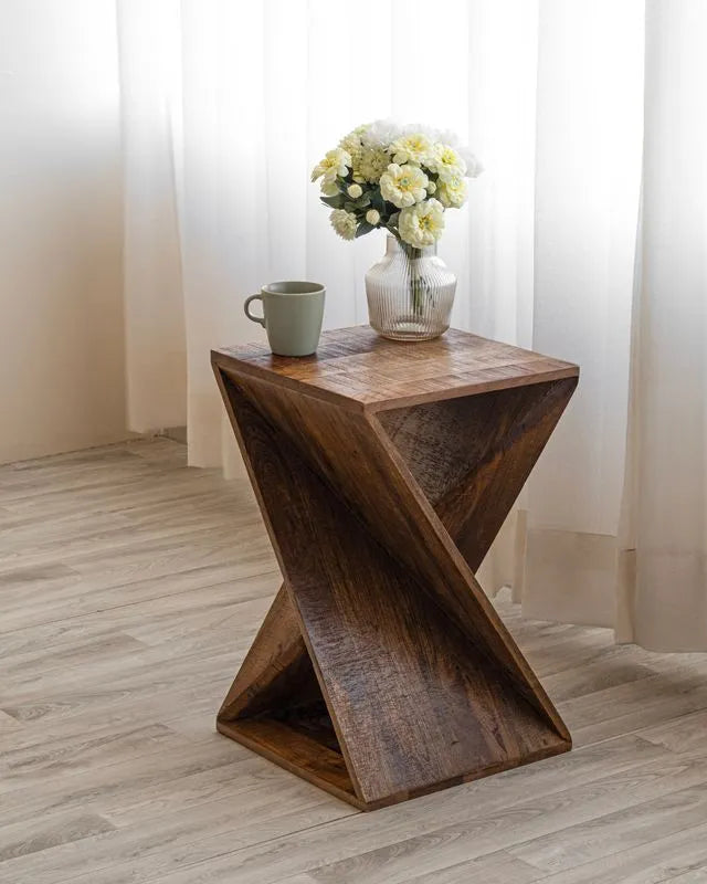 Natural wood twisted end table with a distinctive geometric design, topped with a vase of white flowers and a green mug. Ideal for rustic decor and home use.