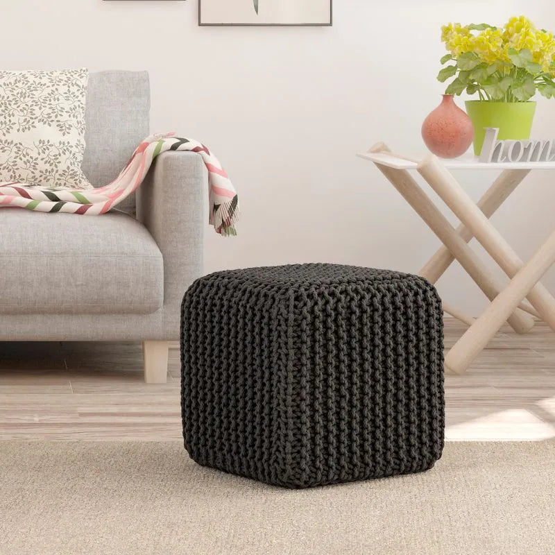 Dark Gray knitted cotton cube pouf in a cozy living room setting, complemented by a sofa, patterned blanket, and a wooden side table.