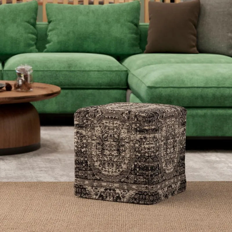 Cube-shaped pouf with a textured black-and-white pattern in a living room, placed in front of a green sofa and a wooden table.