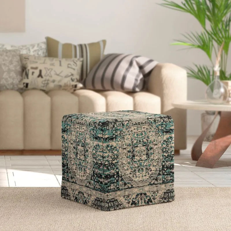 Square pouf with teal and beige medallion pattern, placed in a cozy living room setting with a beige sofa and decorative cushions.