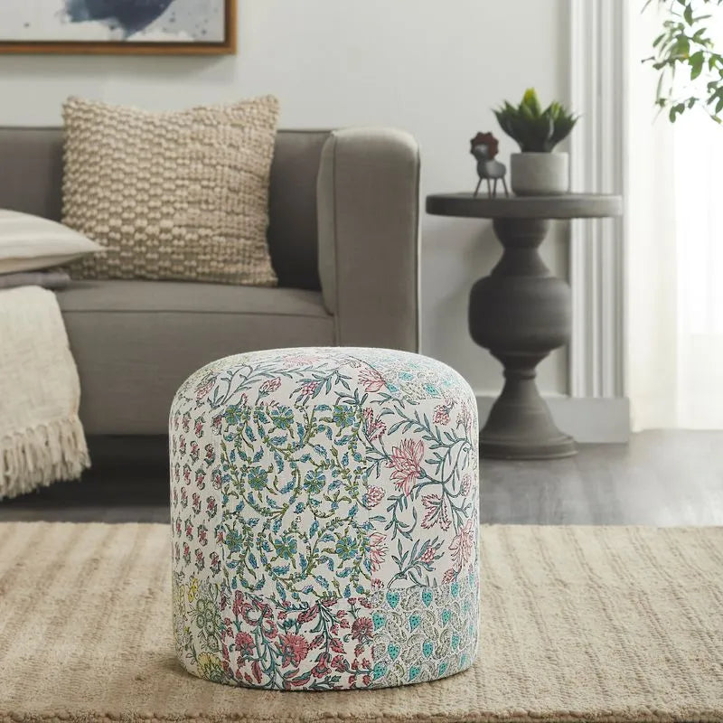 Round pouf with colorful floral patchwork design placed in a cozy living room setting with neutral-toned furniture and decor elements.