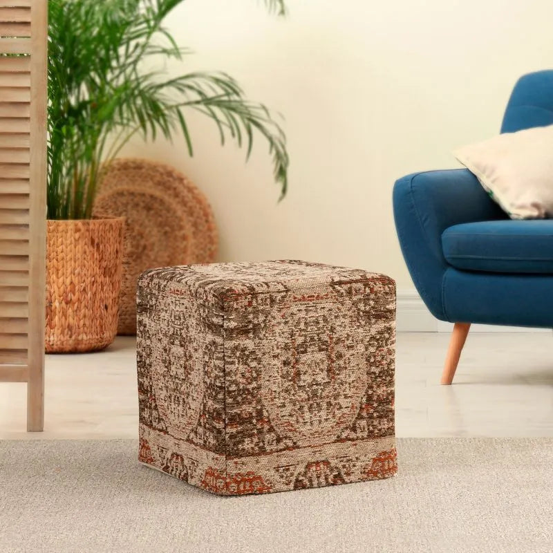 Earth-toned polyester chenille pouf with intricate patterns, placed in a cozy living room, next to a blue chair and woven decor.