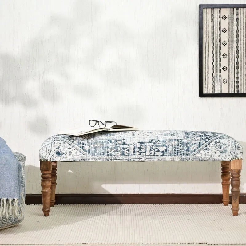 Blue ethnic-inspired upholstered bench with carved wooden legs, placed in a cozy room setting with a blanket and book, ideal for versatile decor.