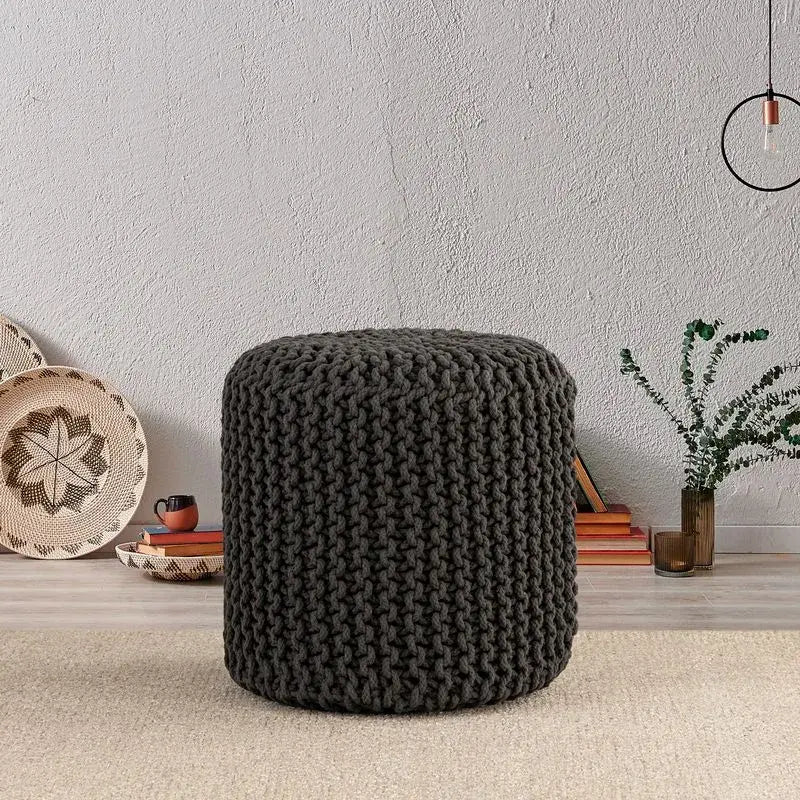 Albany Living cylindrical knitted pouf in dark gray, styled beside earthy decor, ideal for a neutral-toned living space.