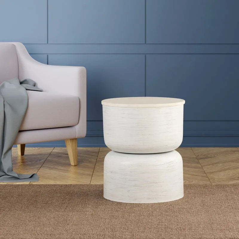 White textured round table in a contemporary room, placed on a brown carpet, with a soft blue background and an armchair nearby.