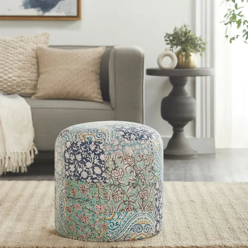 Round pouf with floral patchwork design in blue and green tones, placed in a cozy living room with neutral furniture and soft accents.