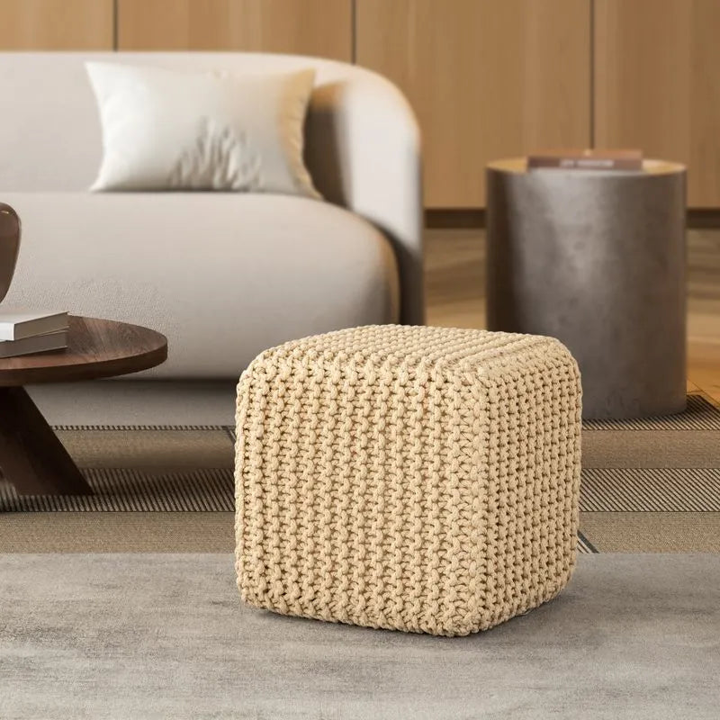 Beige knitted cube pouf placed in a modern living room with a white sofa, wooden coffee table, and neutral decor for a cozy ambiance.